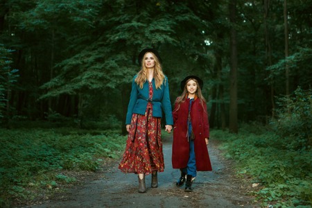 Beautiful mother and daughter are walking through the forest. They hold hands.の写真素材