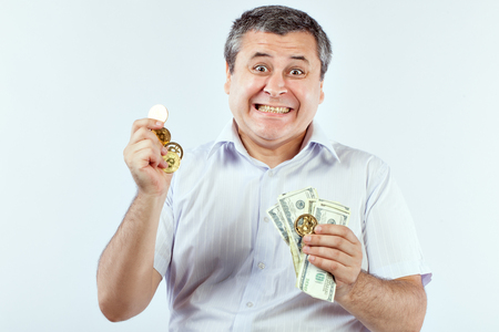 Satisfied man with bitcoins and dollars in his hands. He likes crypto currency.の写真素材