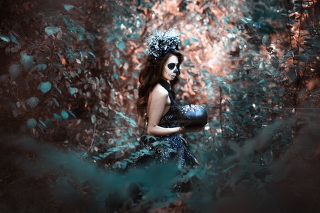 Young woman in costume for Halloween stands with a pumpkin in the forest. Grunge style portrait.の写真素材
