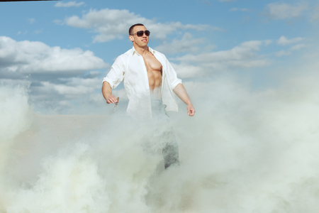 Young athletic man standing in the desert amid the smoke. Man holds cigar.の写真素材