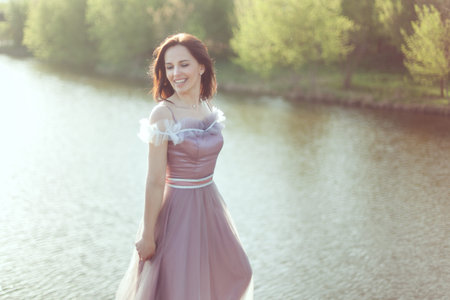 Woman in a purple dress is smiling, she is against the background of nature.