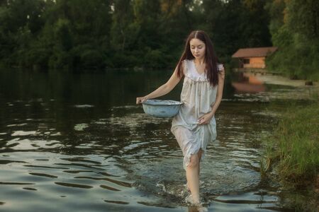 Beautiful young woman walks along the beach in a nightie and holds a basin of linen in her hands.の写真素材