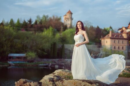 Beautiful young woman in a white dress stands on the banks of the river.の写真素材