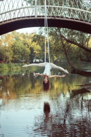 A young acrobat does twine on the canvases upside down. She hangs over the river.の写真素材