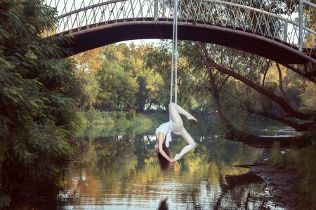 Young acrobat does tricks on white canvases over the river.の写真素材