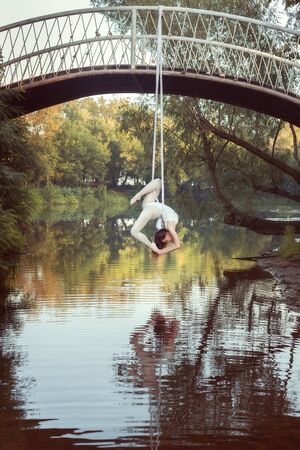 Girl acrobat does tricks on white canvases over the river.の写真素材