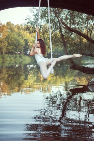 Young athlete in a white suit does acrobatic stunts on white canvases over the river.の写真素材