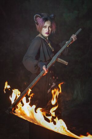 Gloomy female demon mows grass in the darkness with a burning scythe.の写真素材
