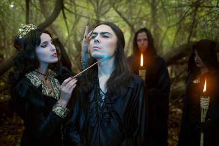 Young woman witch conjures over a young man. She holds magic rituals in the forest.の写真素材