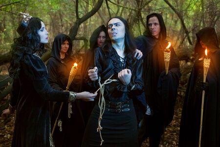 Young woman witch conjures over a man. Around them are people in black with torches.の写真素材