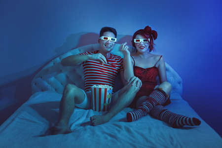 Young man and woman watching a movie at home and eating popcorn.の写真素材