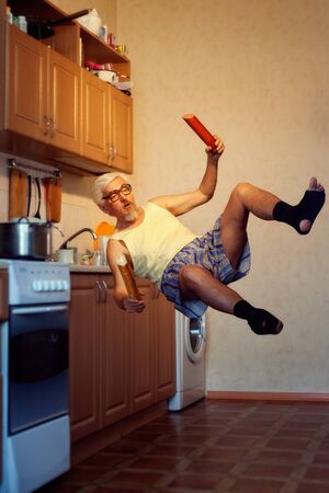 Comic old man flies in the kitchen, in his hands is food. Magic photo in the kitchen.の写真素材