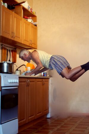 An old man in a dream washes dishes in the kitchen.の写真素材