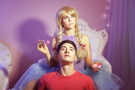 Beautiful woman-doll does makeup, she holds a brush in her hands. At her feet sits a male-doll.の写真素材