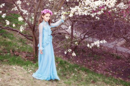 Beautiful young girl near a magnolia tree. She has a wreath of flowers on her head.の写真素材