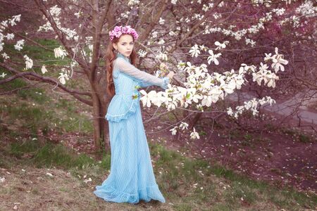 Cute girl near the magnolia tree. She has a wreath of flowers on her head.の写真素材