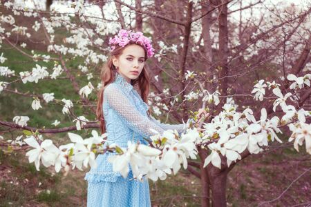 Portrait of a beautiful young girl among blooming magnolia trees in the garden.の写真素材