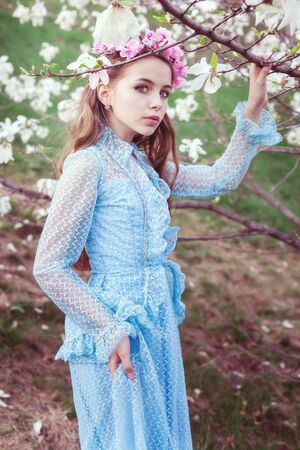 Young cute girl stands in a garden of flowering magnolias.の写真素材