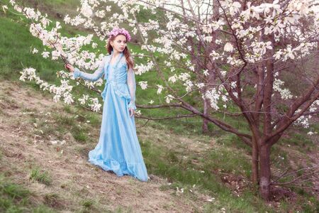 Portrait of a beautiful girl in a long dress in a magnolia garden.の写真素材