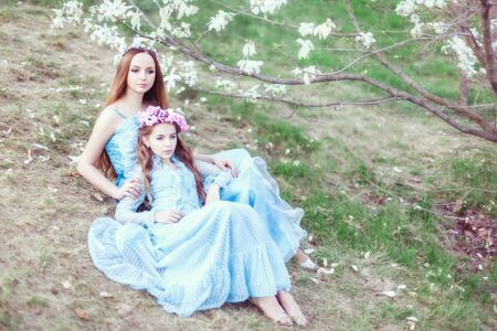 Portrait of a beautiful mother and daughter near a blooming magnolia in the garden.の写真素材
