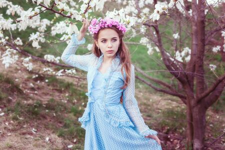 Portrait of a cute girl with blue eyes near a blooming magnolia.の写真素材