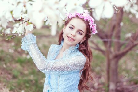 Cute girl with blue eyes stands near the magnolia tree and smiles.の写真素材