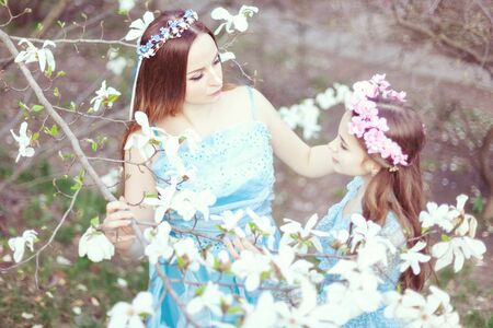 Portrait of beautiful mother and daughter among flowering magnolias in the garden.の写真素材