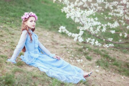 Cute girl sitting on the grass near a blooming magnolia in the garden.の写真素材