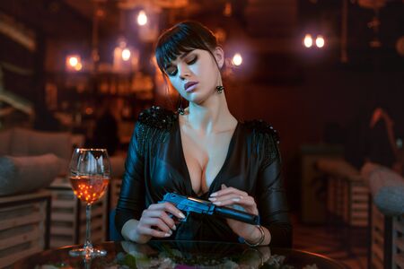 Sexy young woman sits at a table and holds a gun in her hands.の写真素材