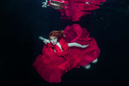 Woman in a red dress swims underwater. She levitates fabulously under water.の写真素材