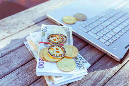 There are bitcoins money and a laptop on the table. Bitcoin coins lie on paper euros.の写真素材