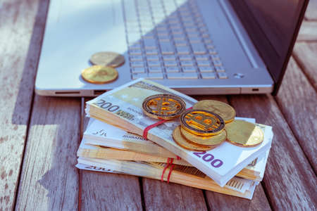 There are bitcoins money and a laptop on the table. Bitcoin coins lie on paper euros.の写真素材
