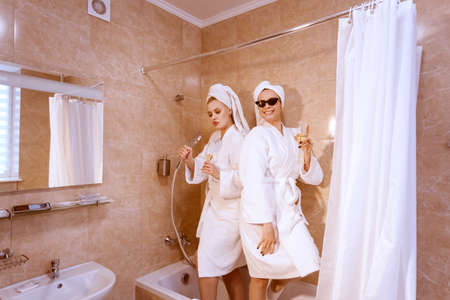 The girls are fooling around in the bathroom. They have fun and sing in the shower.の写真素材
