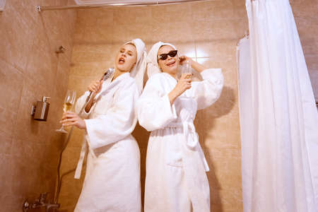 The girls are fooling around in the bathroom. They have fun and sing in the shower.の写真素材