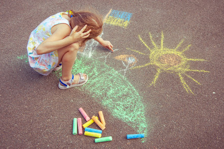 Ukrainian girl child draws children's drawings with chalk on the pavement.の写真素材