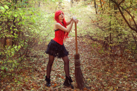 Young and beautiful witch woman with a broom in the autumn forest.の写真素材