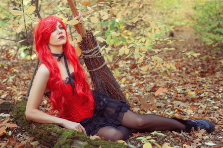 Young and beautiful witch woman with a broom in the autumn forest.の写真素材