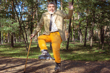 Funny old man is roller skating in the park. An active grandfather with a walking stick dances and makes faces. Grandfather with a white beard.の写真素材