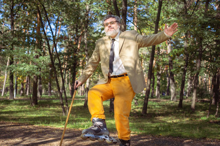 Funny old man is roller skating in the park. An active grandfather with a walking stick dances and makes faces. Grandfather with a white beard.の写真素材
