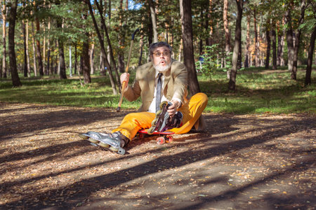 Funny old man is roller skating in the park. An active grandfather with a walking stick dances and makes faces. Grandfather with a white beard.の写真素材