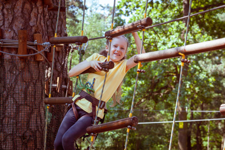 Child in a forest adventure park made of ropes. Children's outdoor climbing entertainment center. Playground for children and sports with a cableway. Sports suspended rope trainer.の写真素材