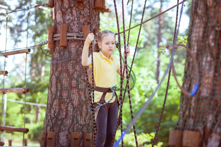 Child in a forest adventure park made of ropes. Children's outdoor climbing entertainment center. Playground for children and sports with a cableway. Sports suspended rope trainer.の写真素材
