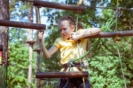 Child in a forest adventure park made of ropes. Children's outdoor climbing entertainment center. Playground for children and sports with a cableway. Sports suspended rope trainer.の写真素材