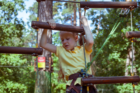 Child in a forest adventure park made of ropes. Children's outdoor climbing entertainment center. Playground for children and sports with a cableway. Sports suspended rope trainer.の写真素材