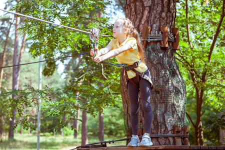Child in a forest adventure park made of ropes. Children's outdoor climbing entertainment center. Playground for children and sports with a cableway. Sports suspended rope trainer.の写真素材