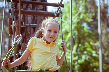 Child in a forest adventure park made of ropes. Children's outdoor climbing entertainment center. Playground for children and sports with a cableway. Sports suspended rope trainer.の写真素材