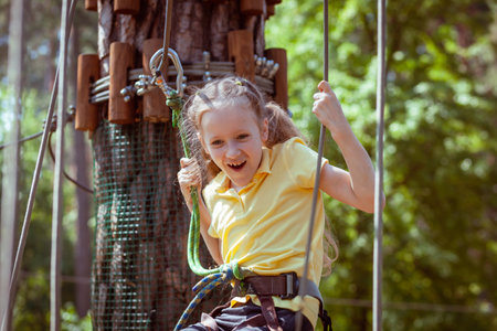 Child in a forest adventure park made of ropes. Children's outdoor climbing entertainment center. Playground for children and sports with a cableway. Sports suspended rope trainer.の写真素材