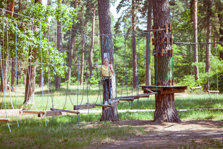 Child in a forest adventure park made of ropes. Children's outdoor climbing entertainment center. Playground for children and sports with a cableway. Sports suspended rope trainer.の写真素材