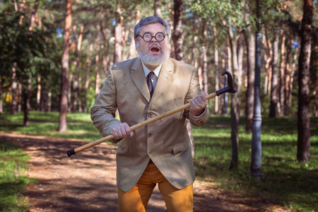 Funny old man with a stick. An elderly man with a walking stick with a funny face. The man has a funny face with a beard.の写真素材
