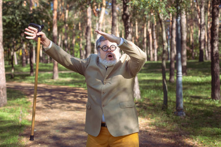 Funny old man with a stick. An elderly man with a walking stick with a funny face. The man has a funny face with a beard.の写真素材